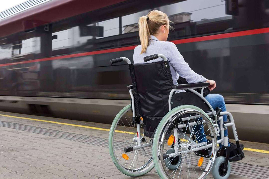 A person in a wheelchair observing a running train at a train platform.