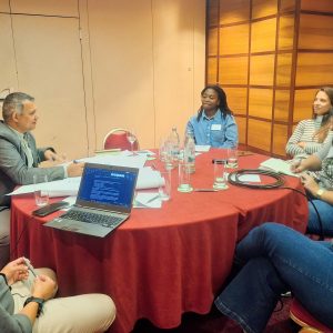 A group of people sitting around a table talking, with one laptop open on the table.