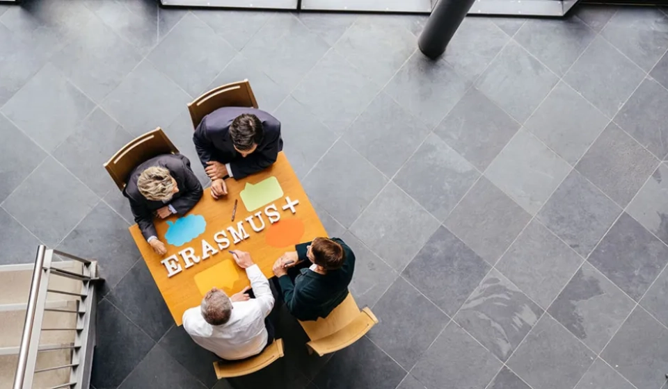 Four people sitting at a desk with the inscription Erasmus+ on top of it. © DAAD/Oliver Reetz