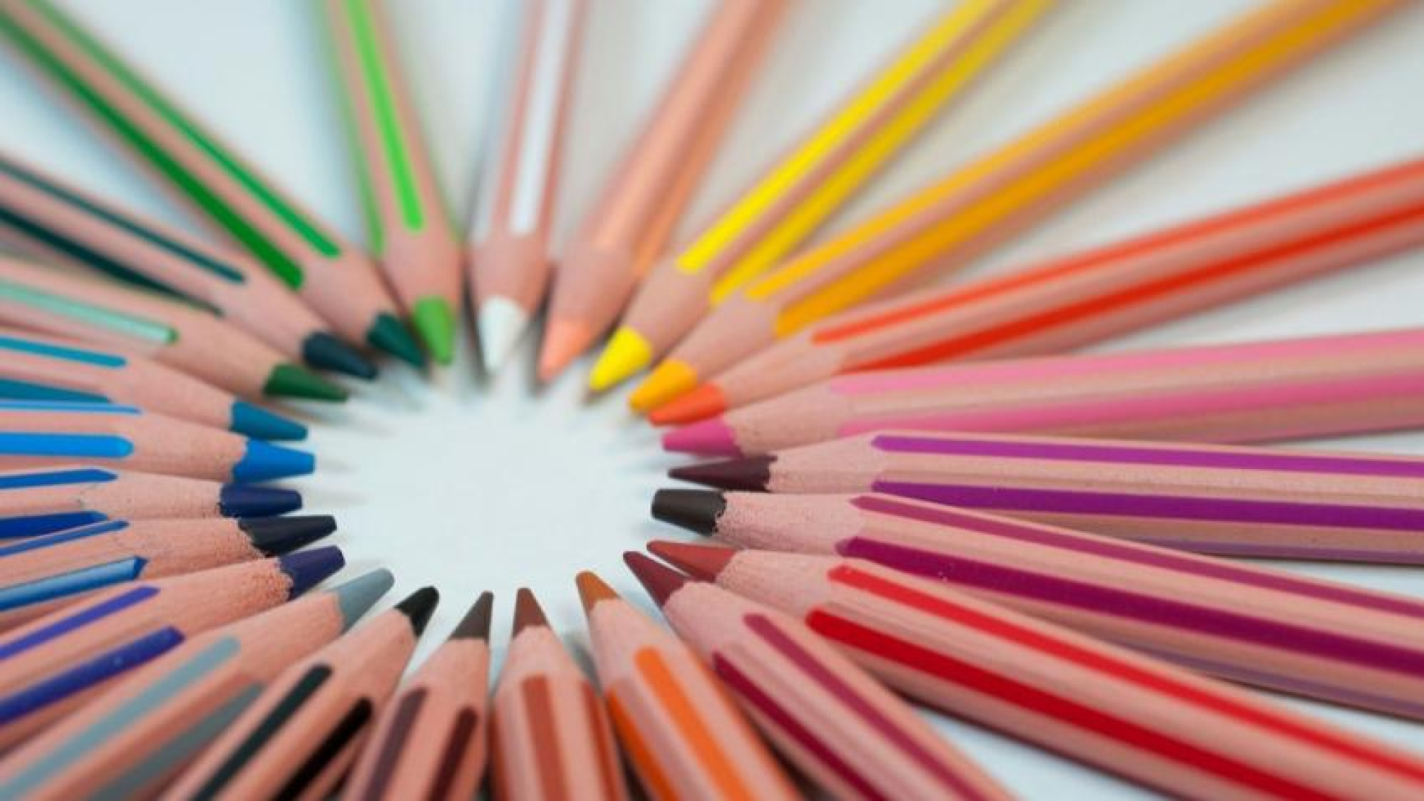 Close up of coloured pencils arranged in a circle, with their sharpened tips pointing inward.